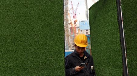 A worker checks his mobile phone as he leaves a construction site in Beijing, China January 16, 2024. 