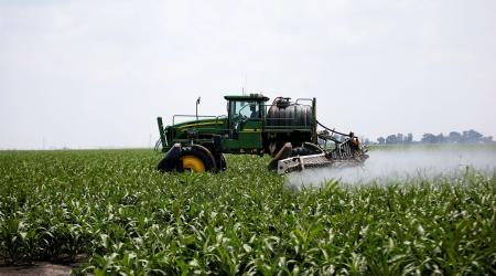 A worker uses a tractor to spray a field of crops. 