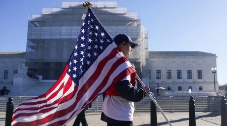 A man carries the US flag outside the US Supreme Court in Washington, DC, as its justices are set to hear oral arguments on President Trump's bid to preserve sweeping tariffs. Picture taken on November 5, 2025.