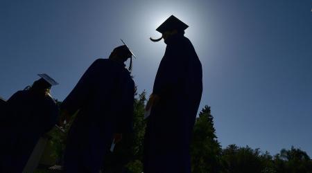 University students in silhouette walk across campus prior to the commencement program. 