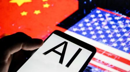 Close up view of a smartphone displaying "AI" (Artificial Intelligence) in front of blurred flags of the United States and China, illustrating technological competition between the two countries. June 2026. 