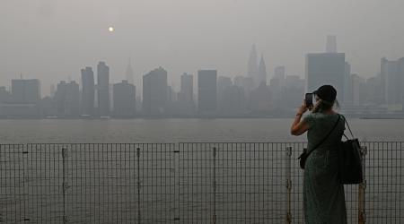 A woman takes a picture of New York City's midtown skyline that is shrouded in smoke coming from the Canadian wildfires. 