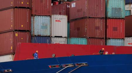 Workers are seen in front of shipping containers stacked on a container ship. REUTERS/Loren Elliott