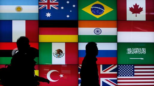 Media workers from a broadcasting station walk past a screen showing flags of the participating countries at the G20 summit.  