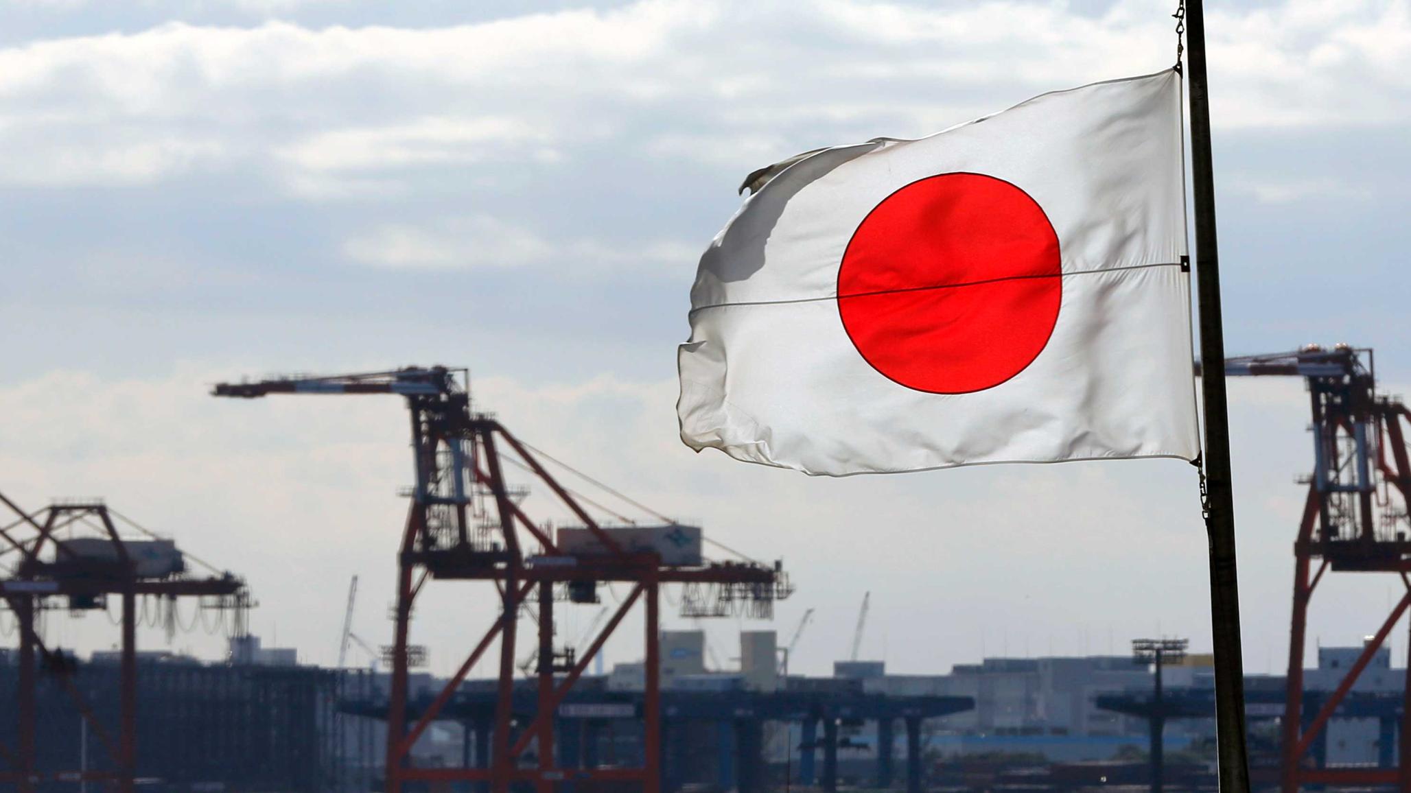 A Japanese flag flutters in front of a shipping container area at a port in Tokyo, Japan. 