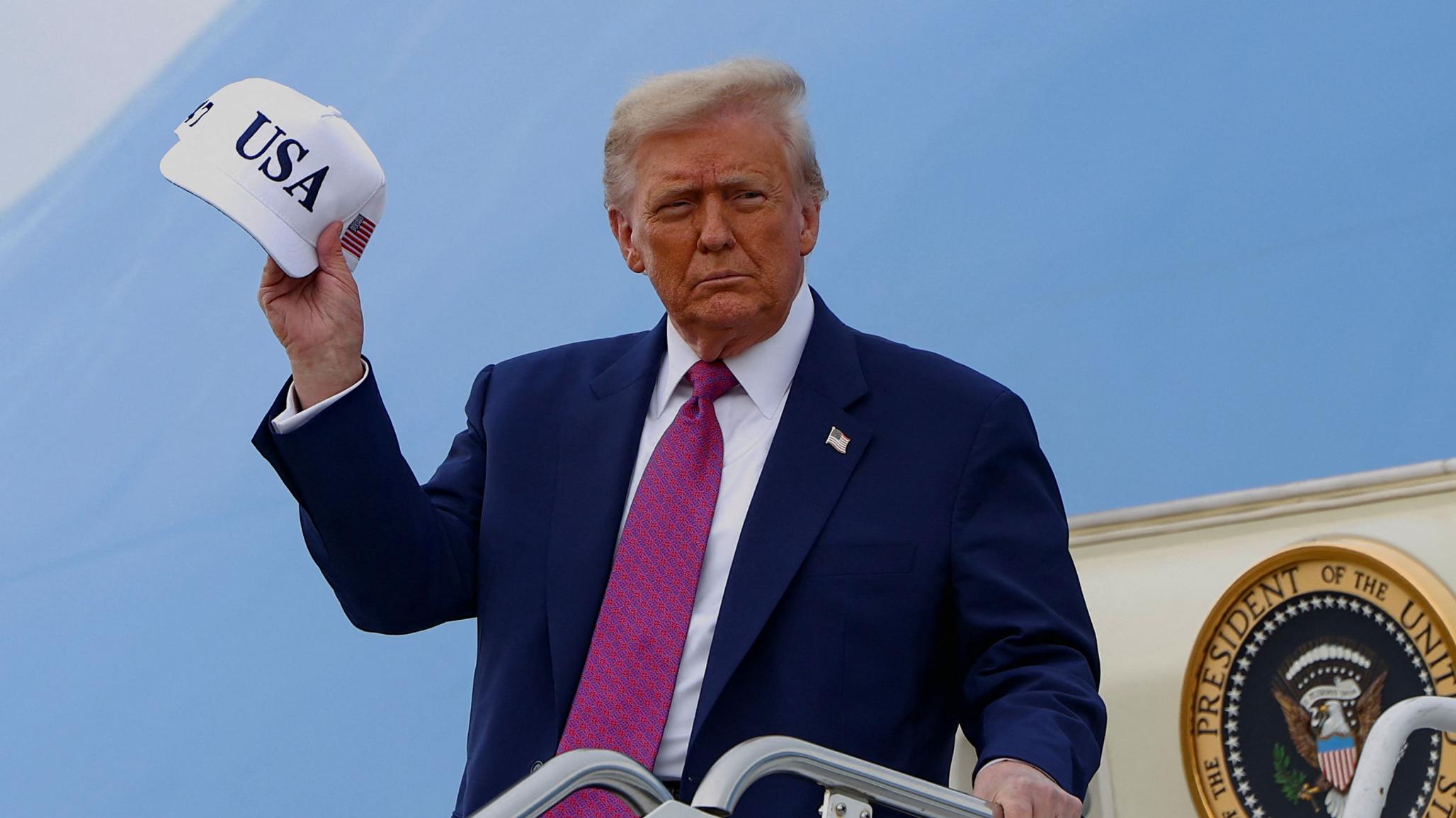 President Donald Trump holds a USA hat as he disembarks Air Force One. Picture taken on June 10, 2025. 