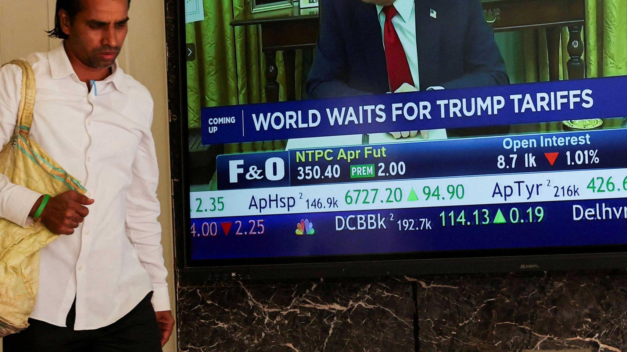 A man walks past a screen displaying US President Donald Trump in the Oval Office speaking of his tariff plans. Photo taken in Mumbai, India on April 2, 2025. 