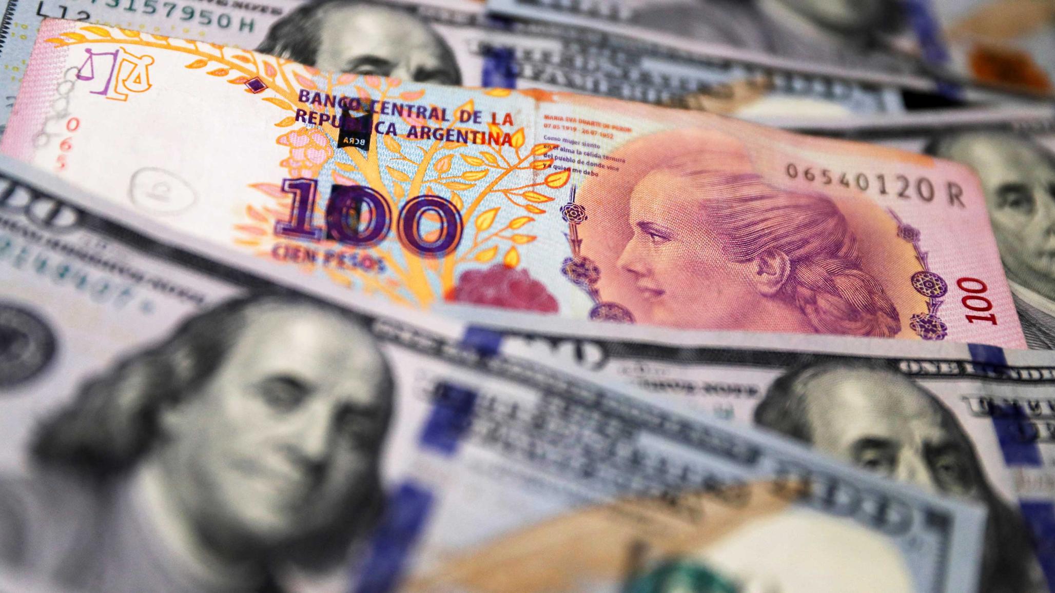 A one hundred Argentine peso bill sits on top of several one hundred US dollar bills in this photo illustration, taken on October 17, 2022. 