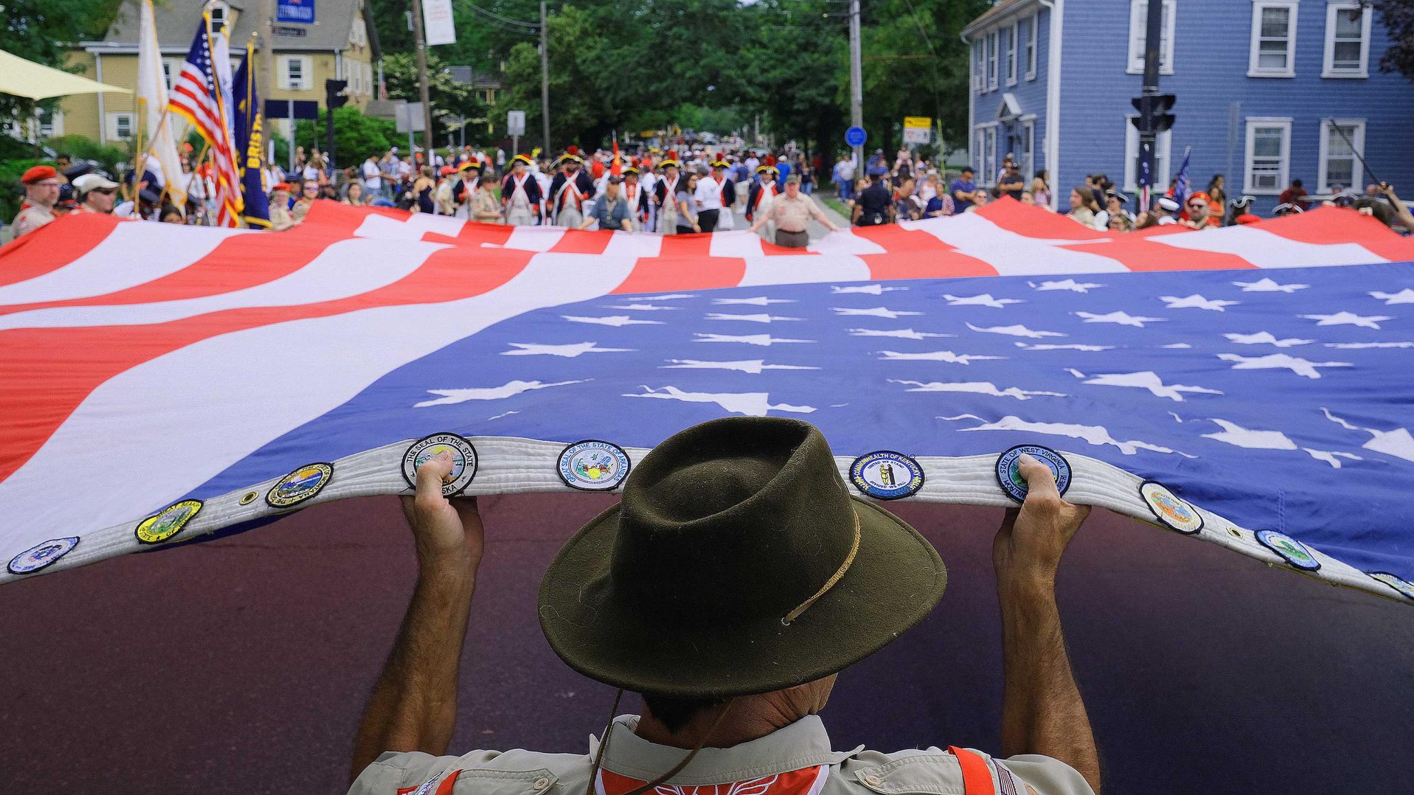 People help to stretch the American Flag out to begin the annual 4th of July celebration parade in Bristol, Rhode Island. July 2021. 