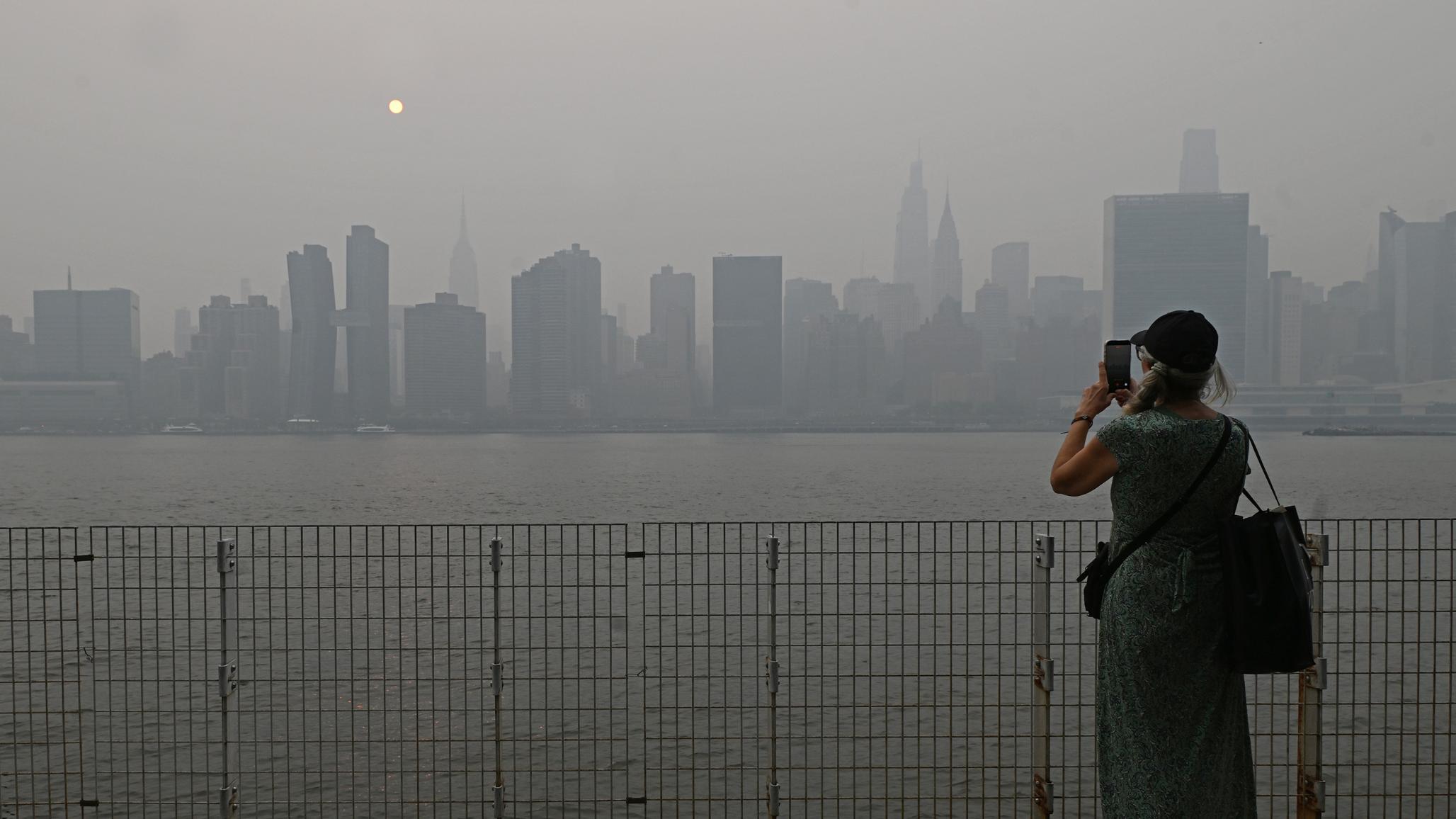 A woman takes a picture of New York City's midtown skyline that is shrouded in smoke coming from the Canadian wildfires. 