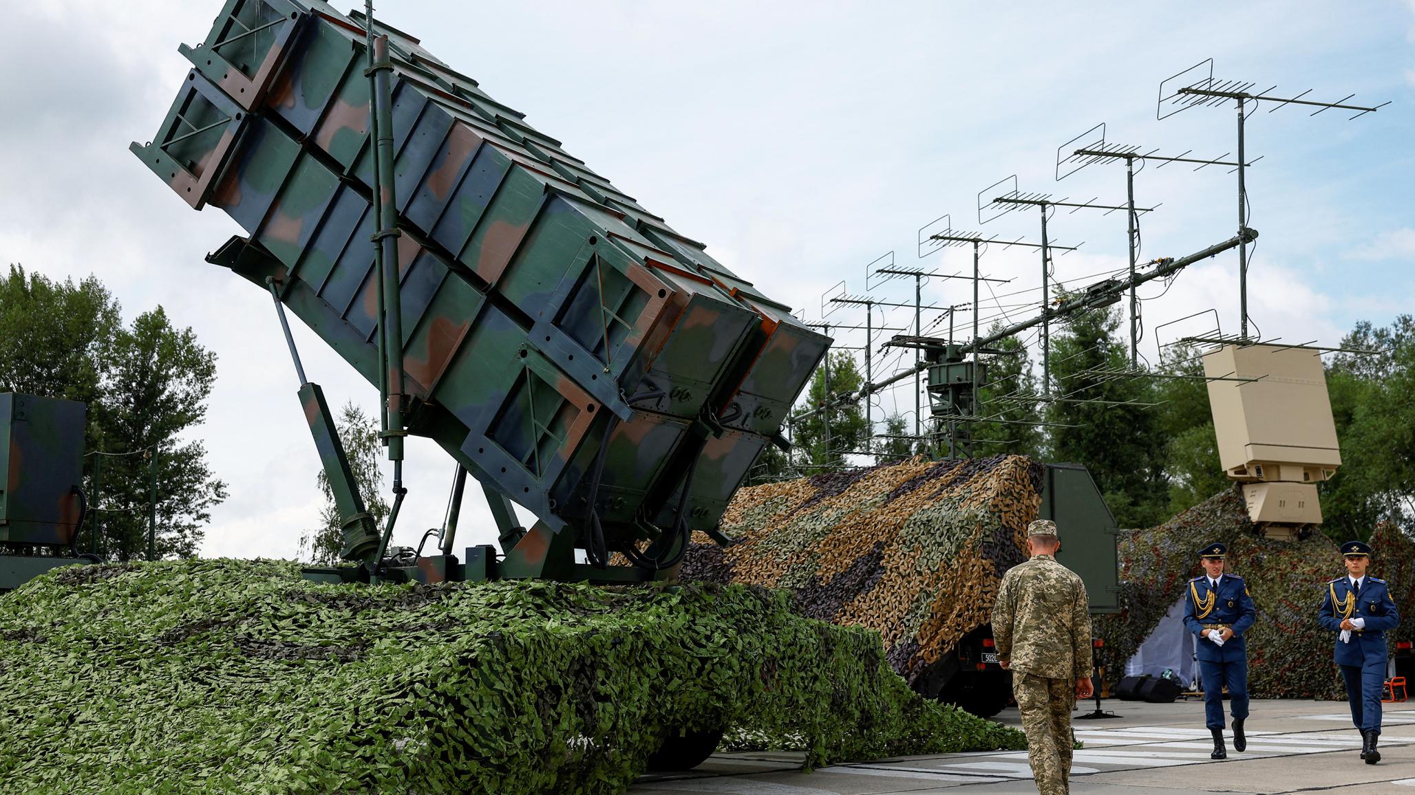 Ukrainian service members walk next to a launcher of a defense system. 