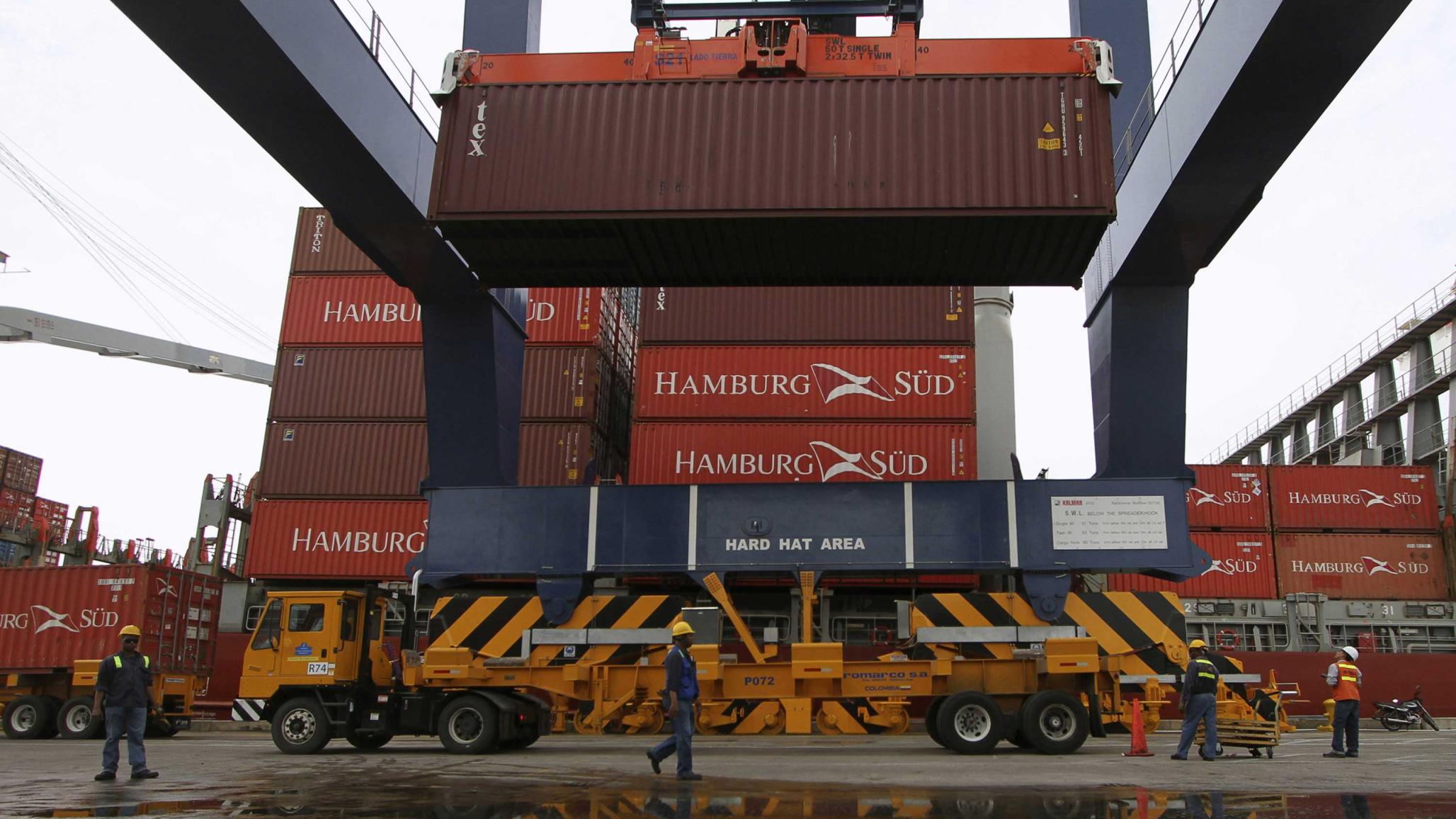 A crane loads a truck with a container as workers supervise the operation at the Port of Cartagena, Colombia.